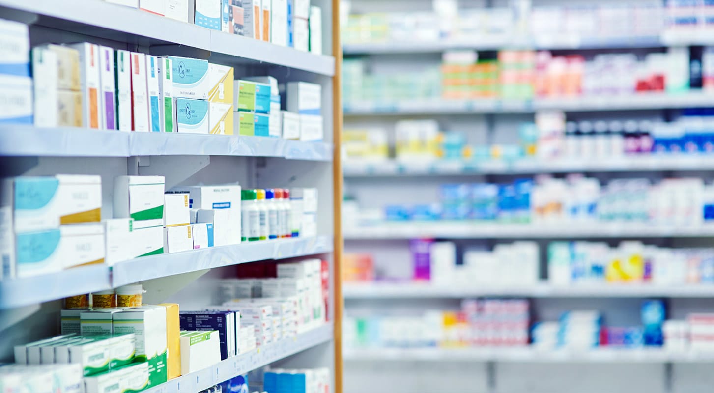 Shelves fully stocked with various boxes of prescription and over-the-counter medications in a pharmacy or drug warehouse.